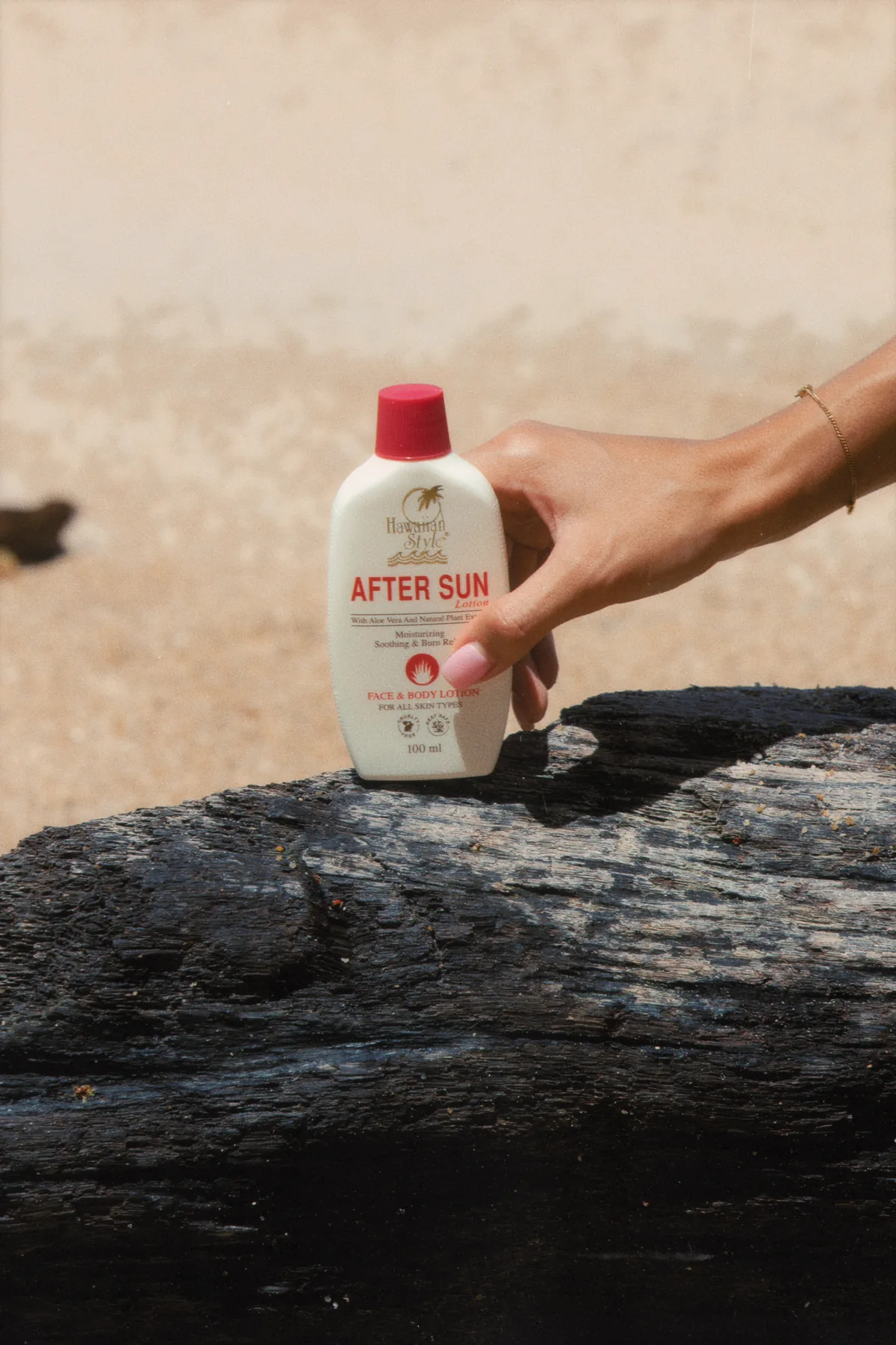 Hawaiian Style After Sun Lotion bottle resting on driftwood on the beach
