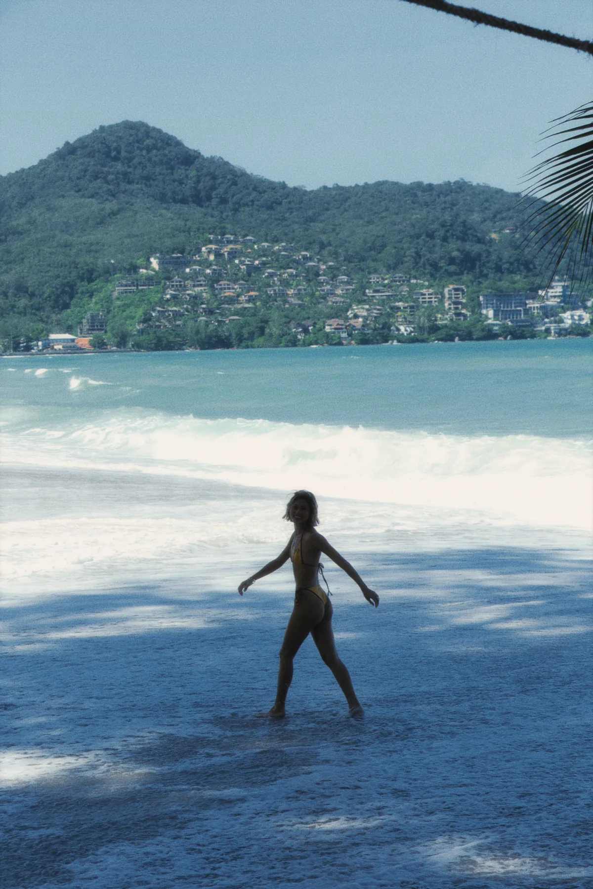 Silhouette of a swimmer walking into the shallows below a forested headland