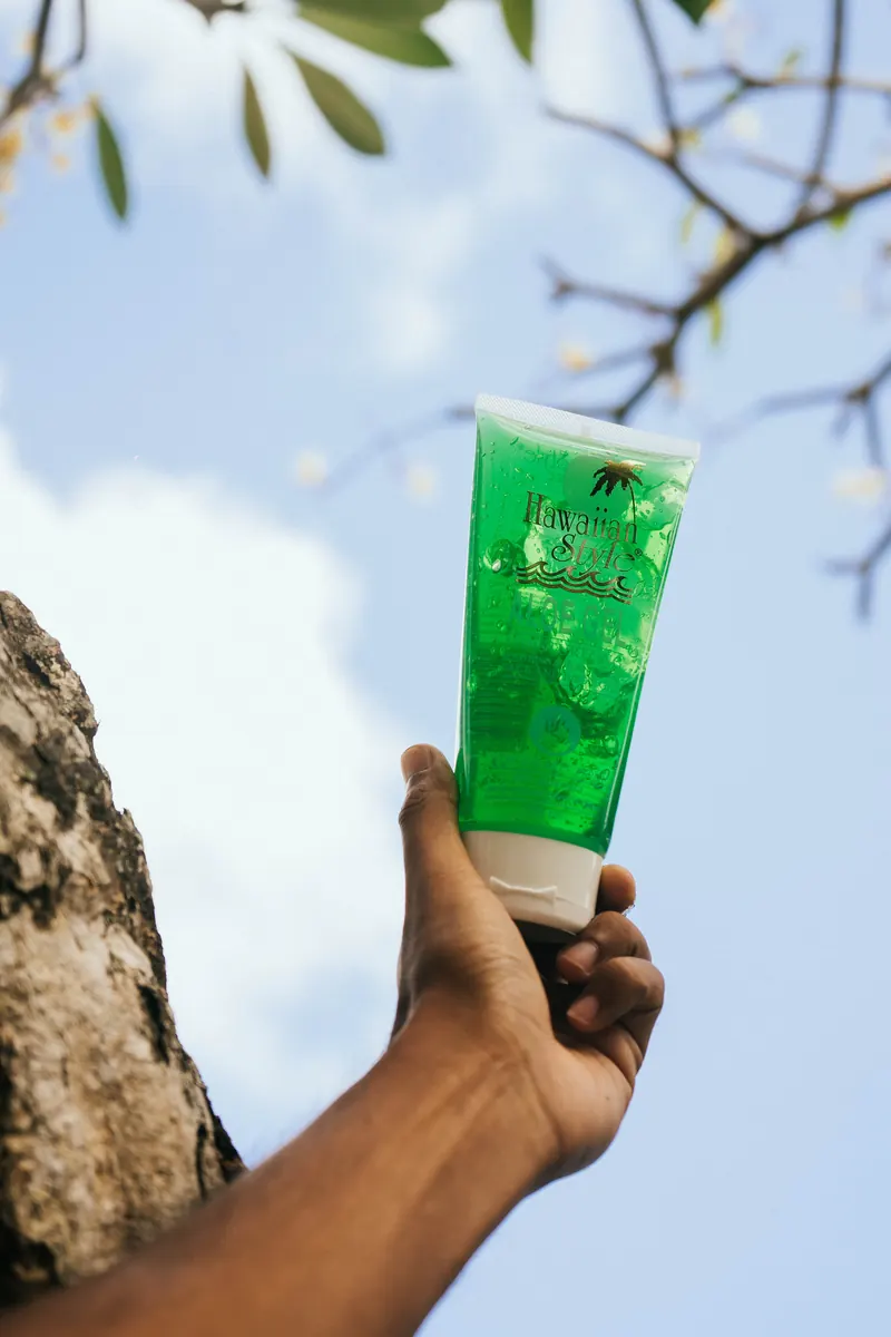Hawaiian Style Aloe Gel held up against the sky beneath a tree branch
