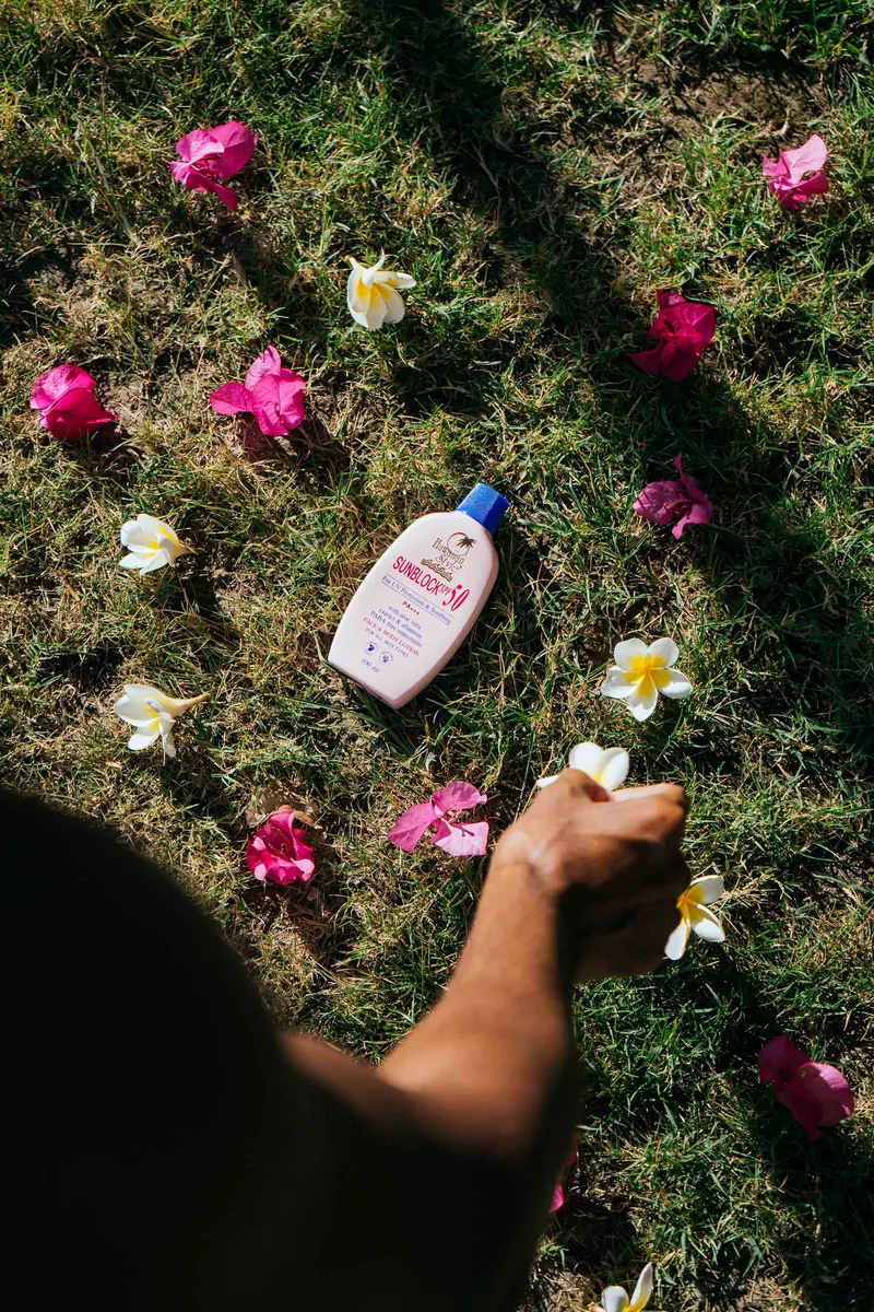 Hawaiian Style Sunblock SPF 50 lying on grass scattered with frangipani and bougainvillea flowers