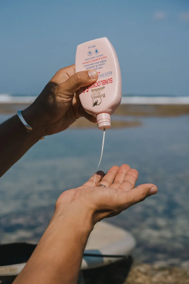 Hawaiian Style Sunblock SPF 50 being poured into a hand with the ocean behind