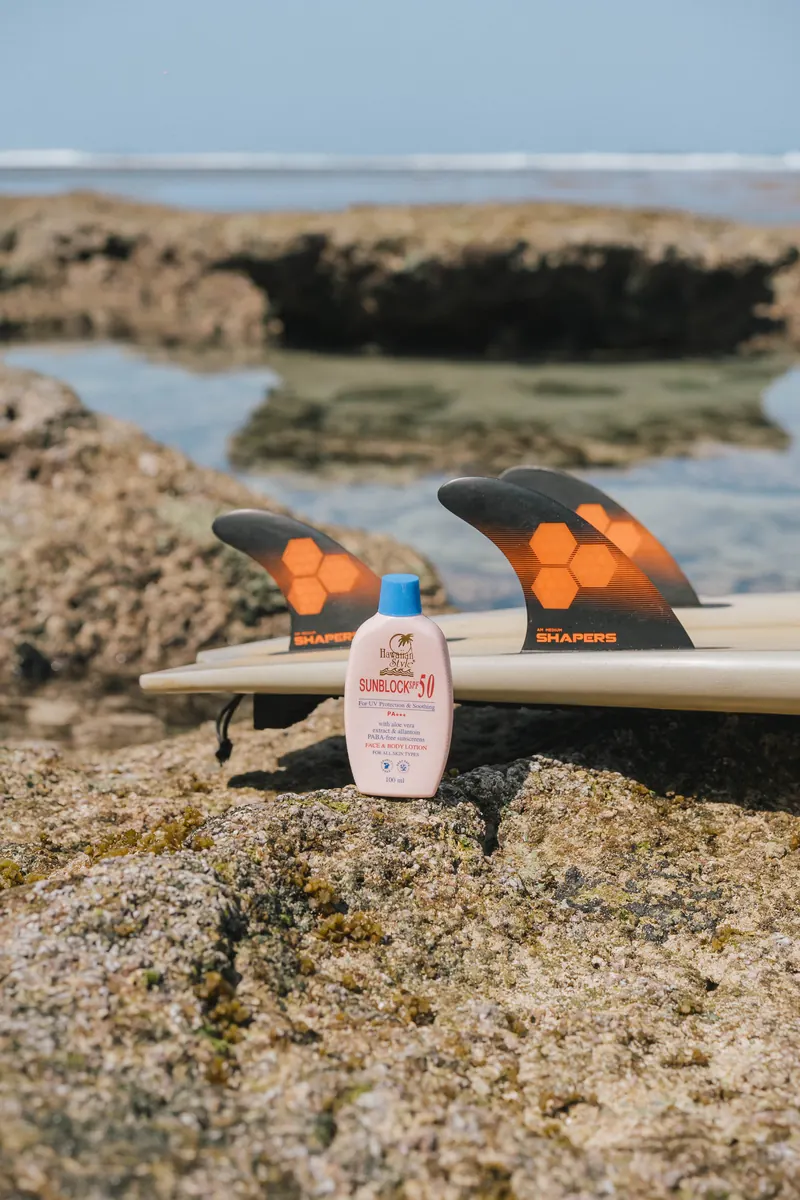 Hawaiian Style Sunblock SPF 50 beside a surfboard fin on a tide-pool rock