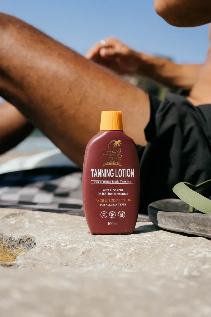 Hawaiian Style Tanning Lotion on a rock beside sunbathing legs