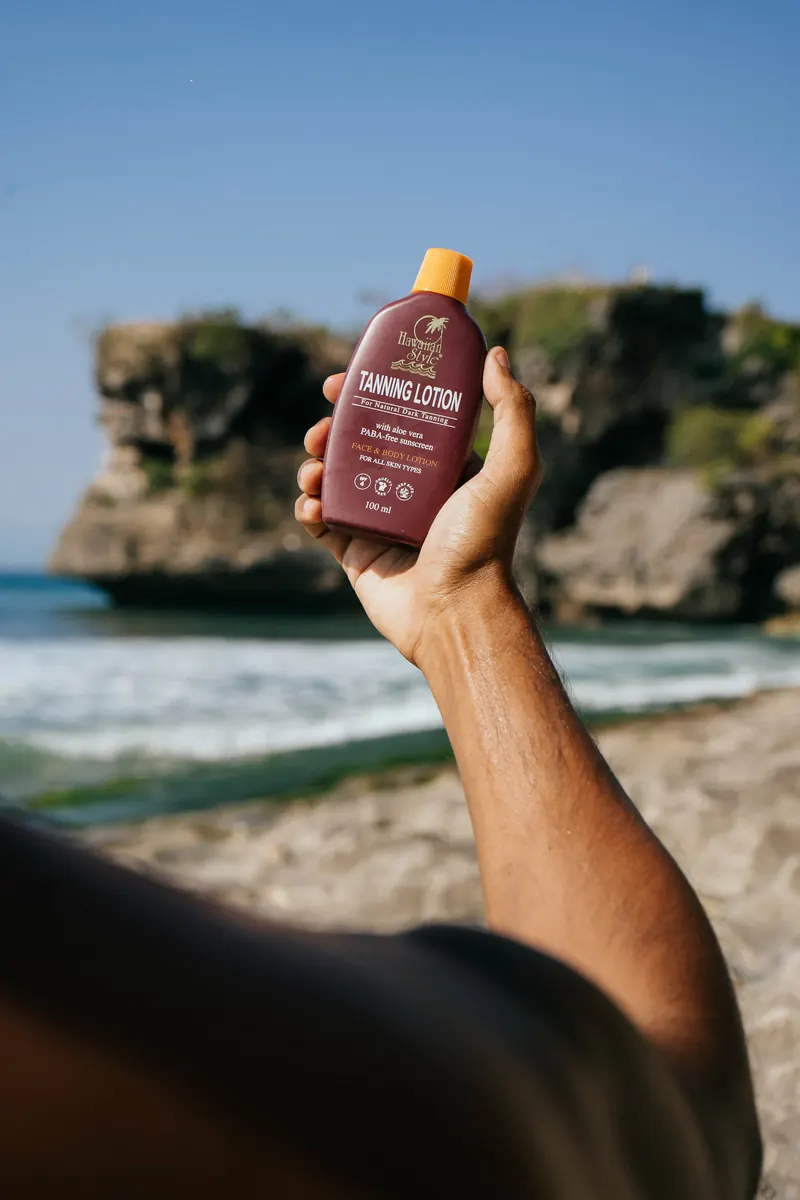 Hawaiian Style Tanning Lotion held up against a cliff cove in Bali