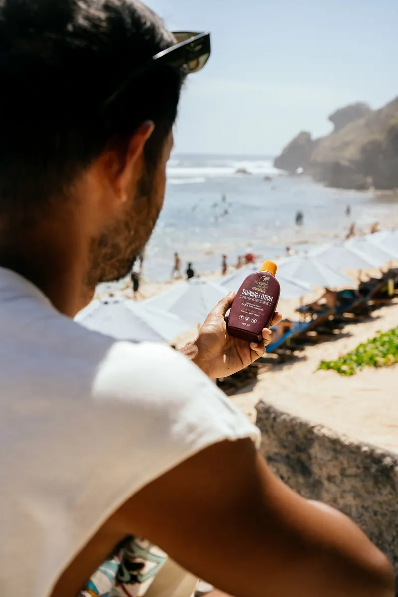 Hawaiian Style Tanning Lotion held overlooking a beach club with umbrellas