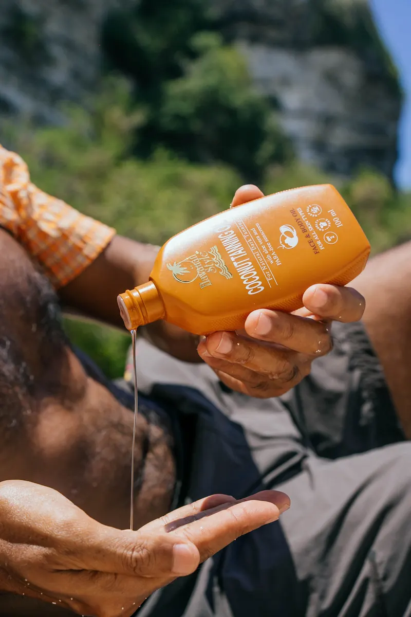 Hawaiian Style Coconut Tanning Oil being poured onto a shoulder with cliffs in the background